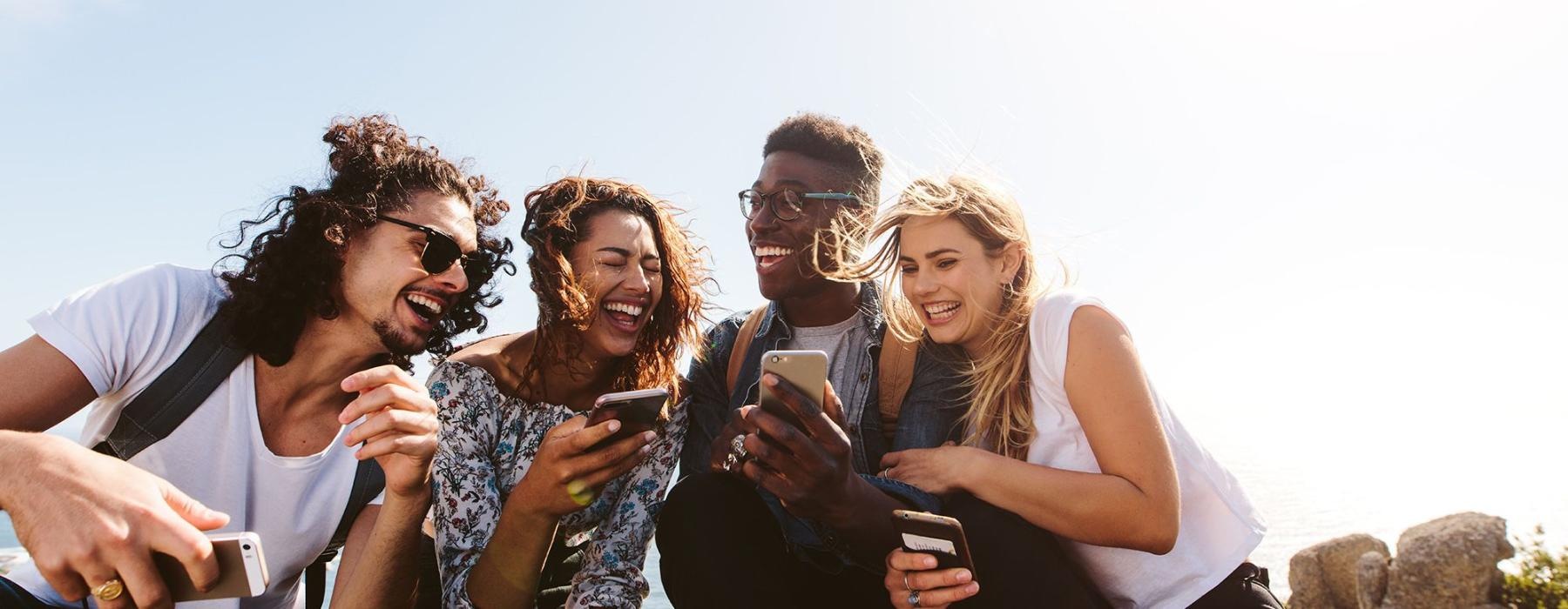 a group of friends sit outside laughing over their cell phones